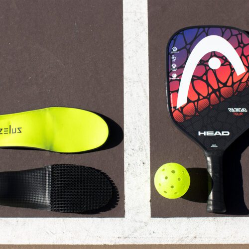 Zelus insoles laying on a pickleball court next to paddle and ball