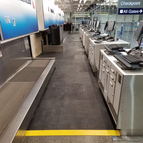 A long walkway of SmartCells is located behind a baggage drop off location in an airport.